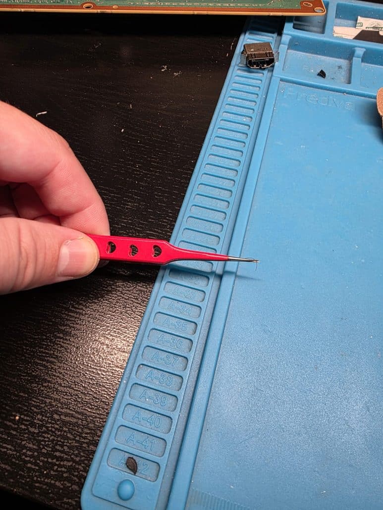 Technician holding a damaged copper track with fine tweezers during an Xbox HDMI port repair