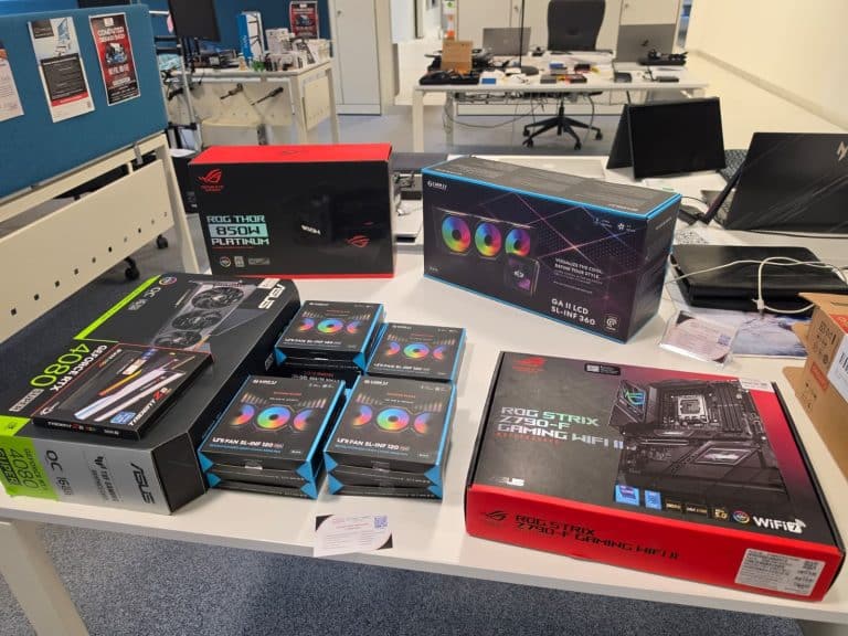 Boxed parts for a custom PC on a workshop table: ASUS RTX 4080 Super graphics card, ROG Thor 850W power supply, Lian Li liquid cooler and RGB fans, ROG Strix Z790-F motherboard and G.Skill memory