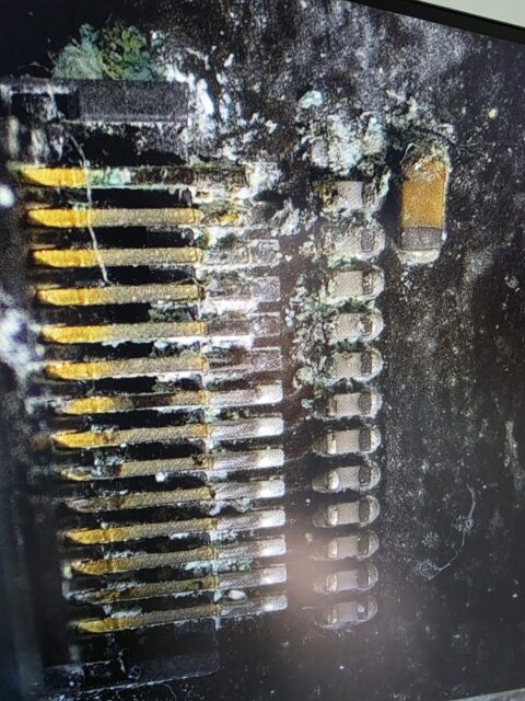 Green corrosion and crystals on connector pins of a liquid-damaged MacBook, seen under the microscope