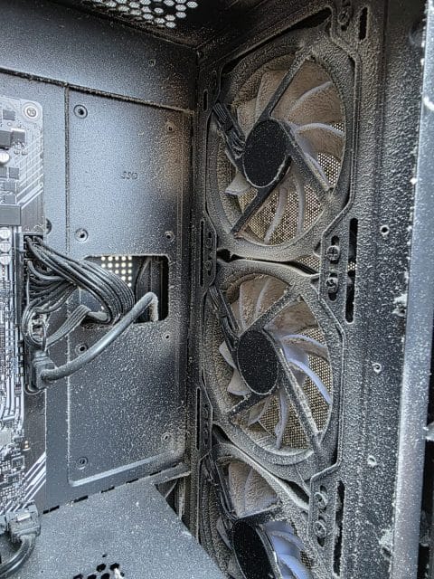 Three PC case fans and the panel behind them covered in dust