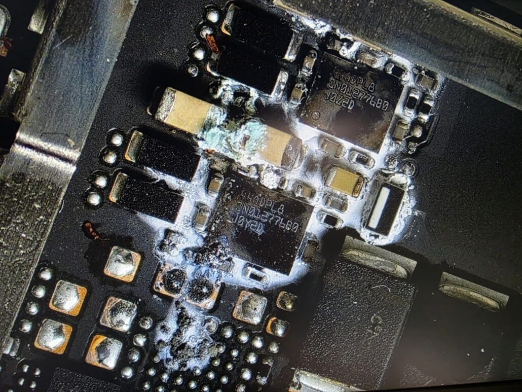 Dried drink residue crystallised around chips on a MacBook logic board, seen under the microscope