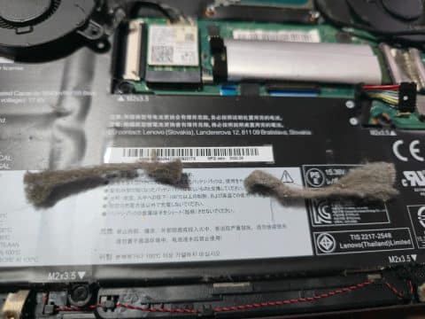 Two lumps of grey dust lying on a laptop battery after being removed from the fan and heatsink