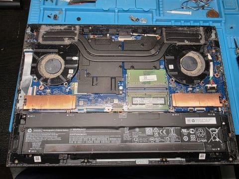 Opened laptop on a repair mat with dust on the two fans and the heatsink vents