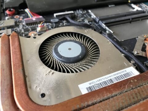 Gaming laptop fan next to heatsink fins blocked with dust