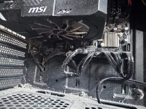 Inside a desktop PC with dust and cobwebs around the graphics card fan and on the case floor