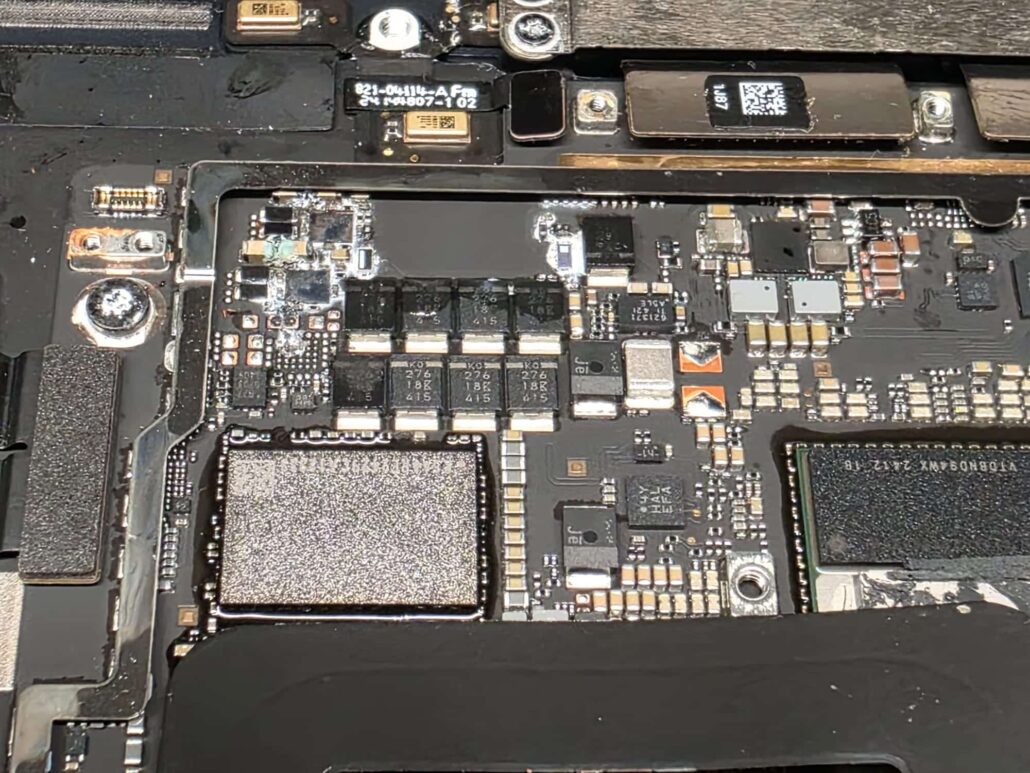Sticky liquid residue around components on a modern MacBook Pro logic board after a spill