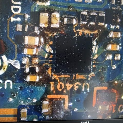 Microscope view of a power delivery chip surrounded by burnt residue and corrosion