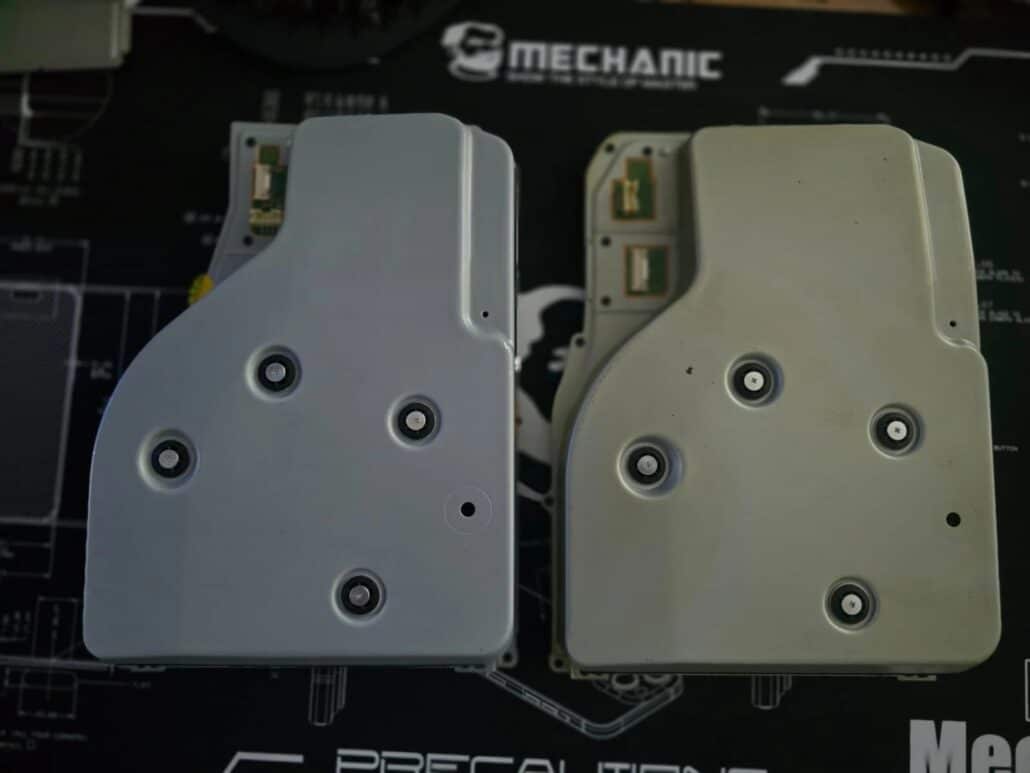 Two PS5 disc drives side by side on the bench: the replacement V2 drive on the left and the customer's old discoloured drive on the right, showing the small circuit board that has to be moved across