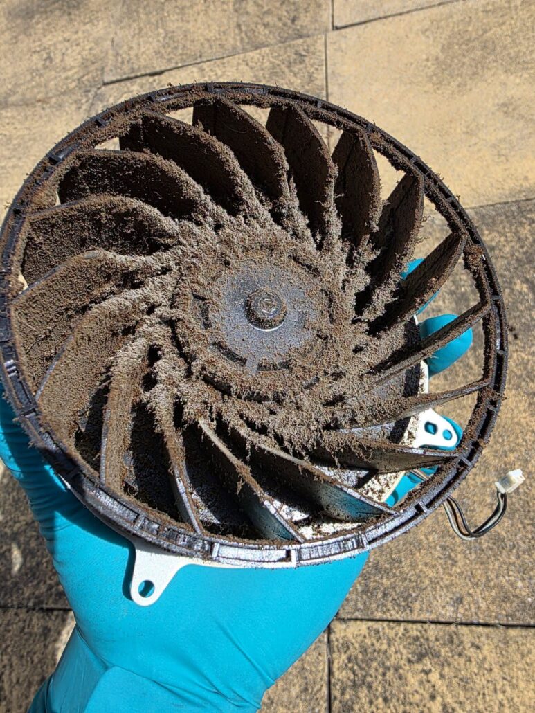 The PS5 fan held in a gloved hand, every blade packed with sticky brown dirt