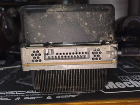 Xbox motherboard assembly lifted out showing the heatsink fins coated in dust